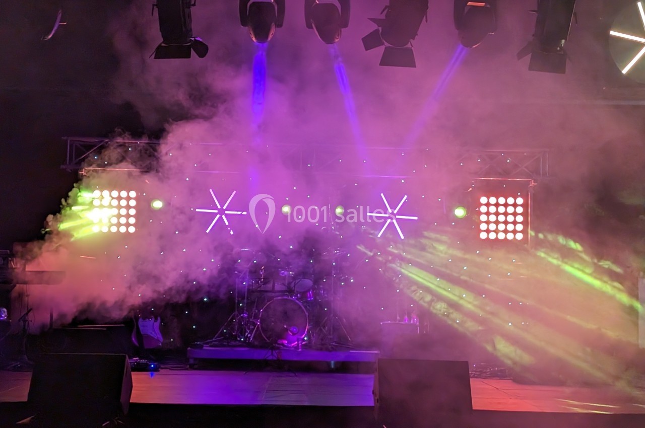 Scène de concert avec éclairage coloré, projecteurs, fumée et instruments de musique en arrière-plan.