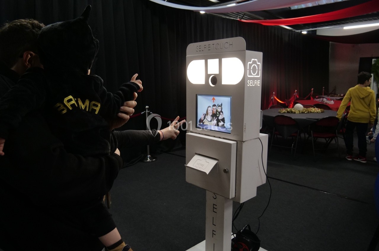 Une borne photo interactive utilisée par des personnes dans un espace intérieur décoré avec des tables et des rideaux.