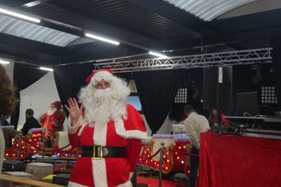 Des enfants colorient des dessins autour d'une table ronde, entourés d'adultes dans un espace intérieur animé.