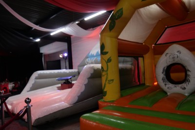 Des enfants colorient des dessins autour d'une table ronde, entourés d'adultes dans un espace intérieur animé.