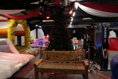 Des enfants colorient des dessins autour d'une table ronde, entourés d'adultes dans un espace intérieur animé.