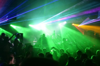 Des enfants colorient des dessins autour d'une table ronde, entourés d'adultes dans un espace intérieur animé.