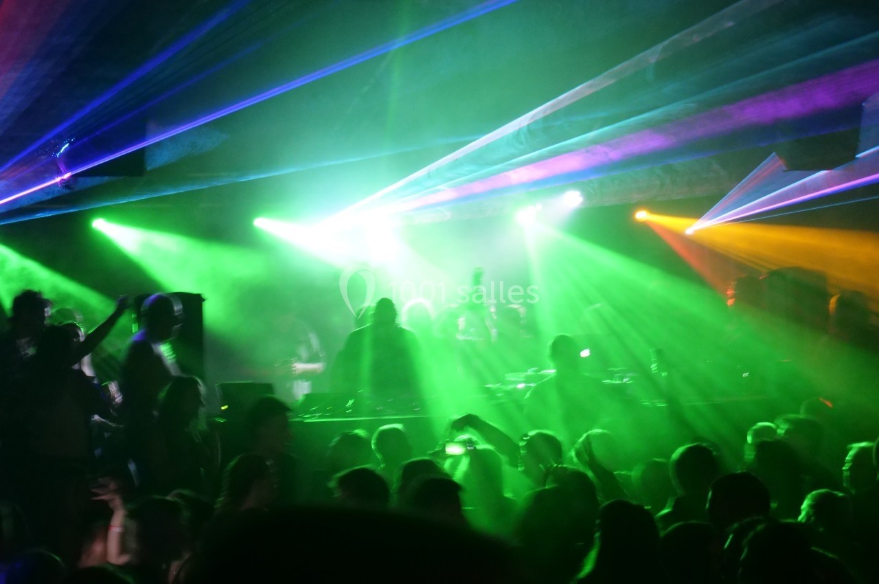 Foule dans une discothèque avec des lumières colorées et des lasers verts, ambiance festive et animée.