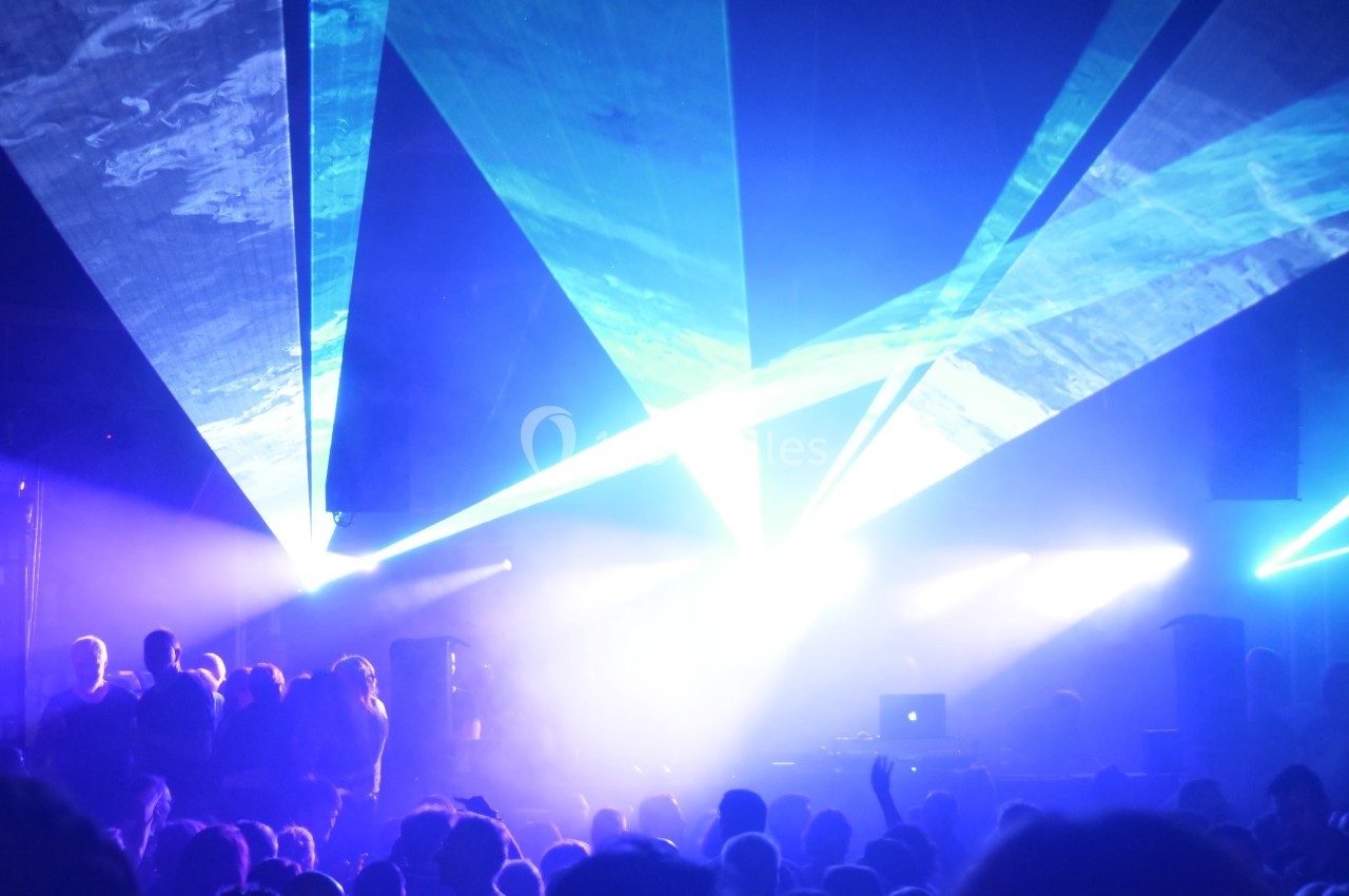Foule dans une salle de concert sombre, éclairée par des faisceaux lumineux bleus et violets provenant de projecteurs.