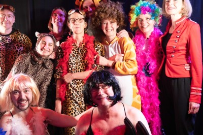 Des enfants colorient des dessins autour d'une table ronde, entourés d'adultes dans un espace intérieur animé.