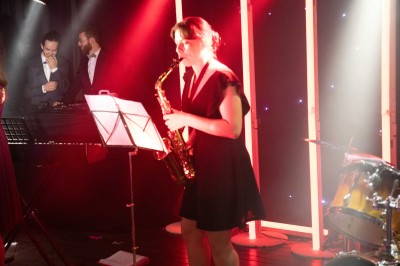Des enfants colorient des dessins autour d'une table ronde, entourés d'adultes dans un espace intérieur animé.