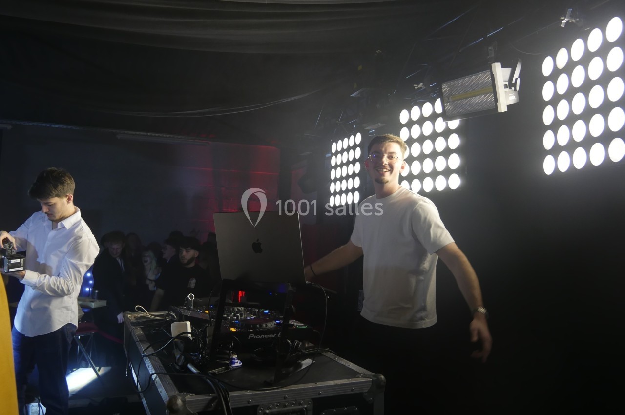 Un DJ souriant devant son équipement, éclairé par des projecteurs, dans une ambiance de soirée.