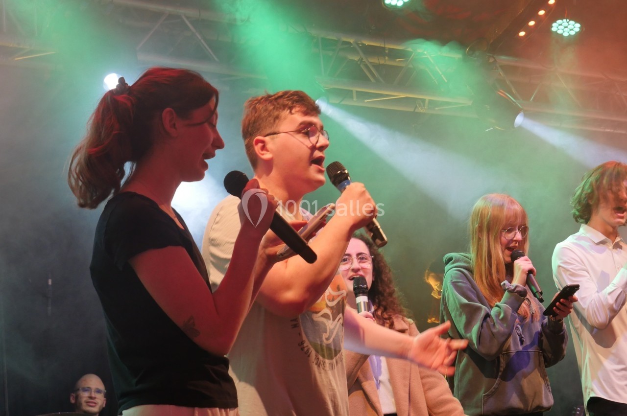 Des chanteurs et chanteuses sur scène, micro en main, éclairés par des projecteurs colorés.