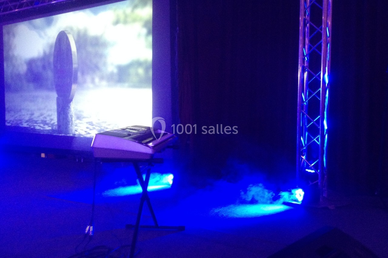 Clavier électronique sur scène avec éclairage bleu et écran de projection affichant une image floue en arrière-plan.