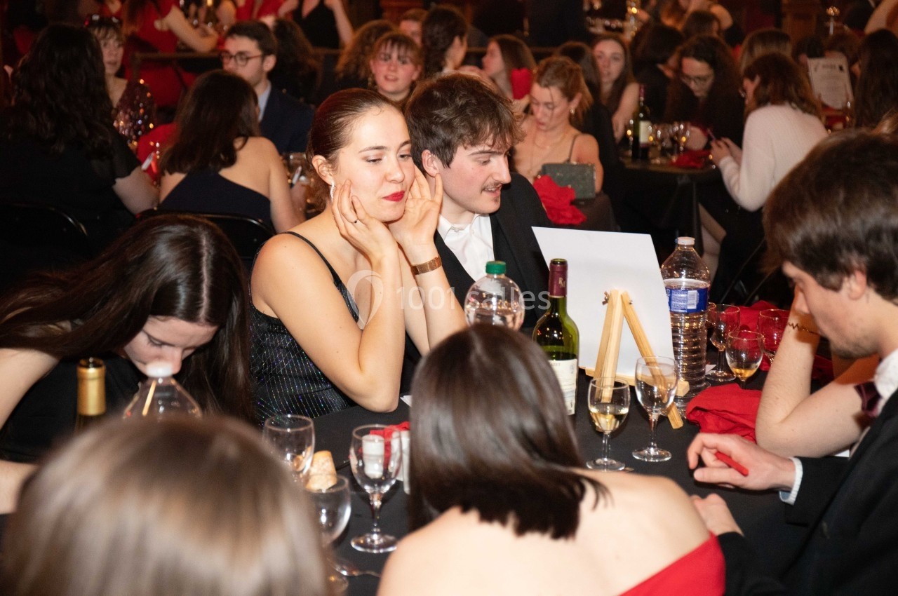 Des personnes assises autour d'une table lors d'un dîner, discutant ou réfléchissant dans une ambiance festive.