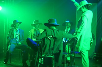 Des enfants colorient des dessins autour d'une table ronde, entourés d'adultes dans un espace intérieur animé.