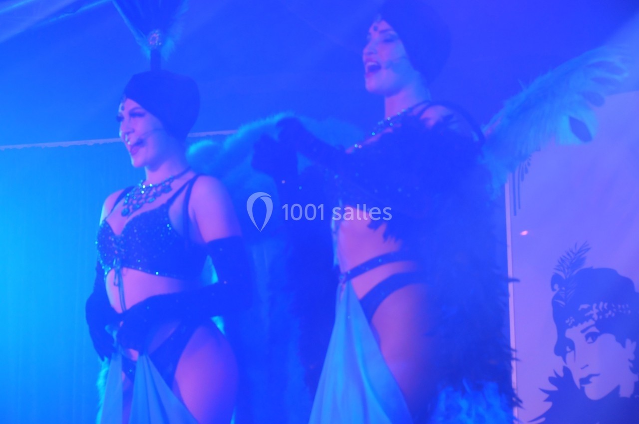 Deux artistes en costumes de cabaret avec plumes et paillettes se produisent sur une scène éclairée en bleu.