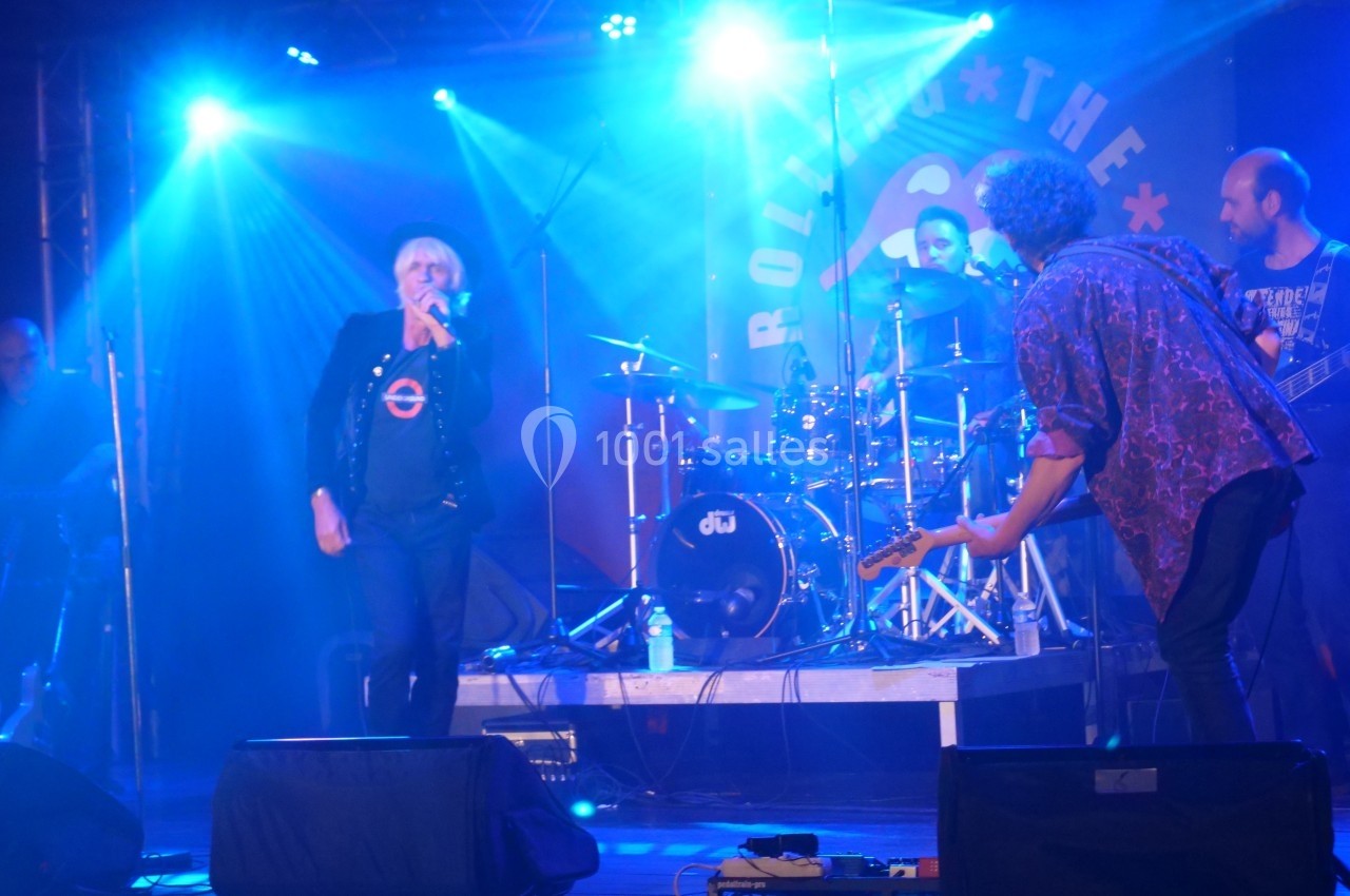 Un groupe de musiciens joue sur scène sous des éclairages bleus, avec un chanteur au centre.