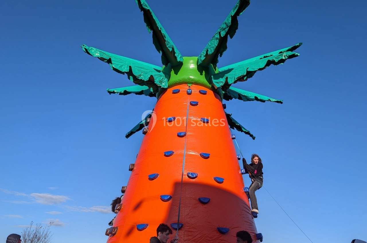 Structure gonflable en forme de carotte géante avec des enfants grimpant sur ses prises d'escalade colorées.