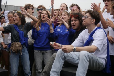 Des enfants colorient des dessins autour d'une table ronde, entourés d'adultes dans un espace intérieur animé.