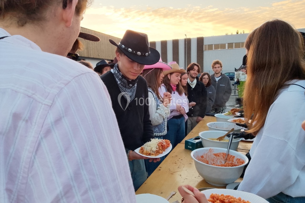 Des personnes font la file pour se servir de la nourriture lors d'un événement en plein air au coucher du soleil.