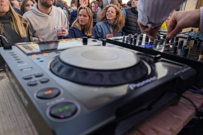 Des enfants colorient des dessins autour d'une table ronde, entourés d'adultes dans un espace intérieur animé.
