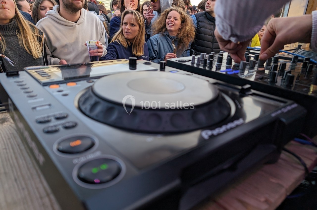 Vue rapprochée d'une table de mixage en usage lors d'un événement en plein air, avec un public en arrière-plan.