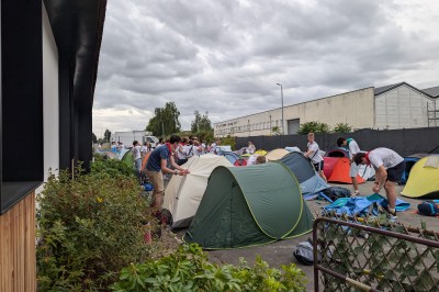 Des enfants colorient des dessins autour d'une table ronde, entourés d'adultes dans un espace intérieur animé.