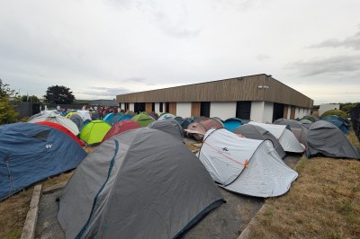 Des enfants colorient des dessins autour d'une table ronde, entourés d'adultes dans un espace intérieur animé.