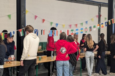 Des enfants colorient des dessins autour d'une table ronde, entourés d'adultes dans un espace intérieur animé.