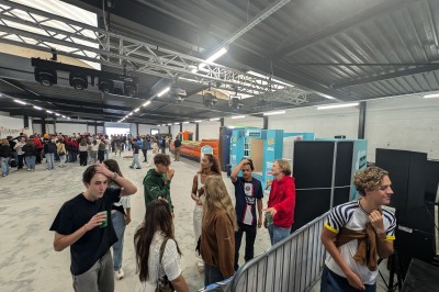 Des enfants colorient des dessins autour d'une table ronde, entourés d'adultes dans un espace intérieur animé.