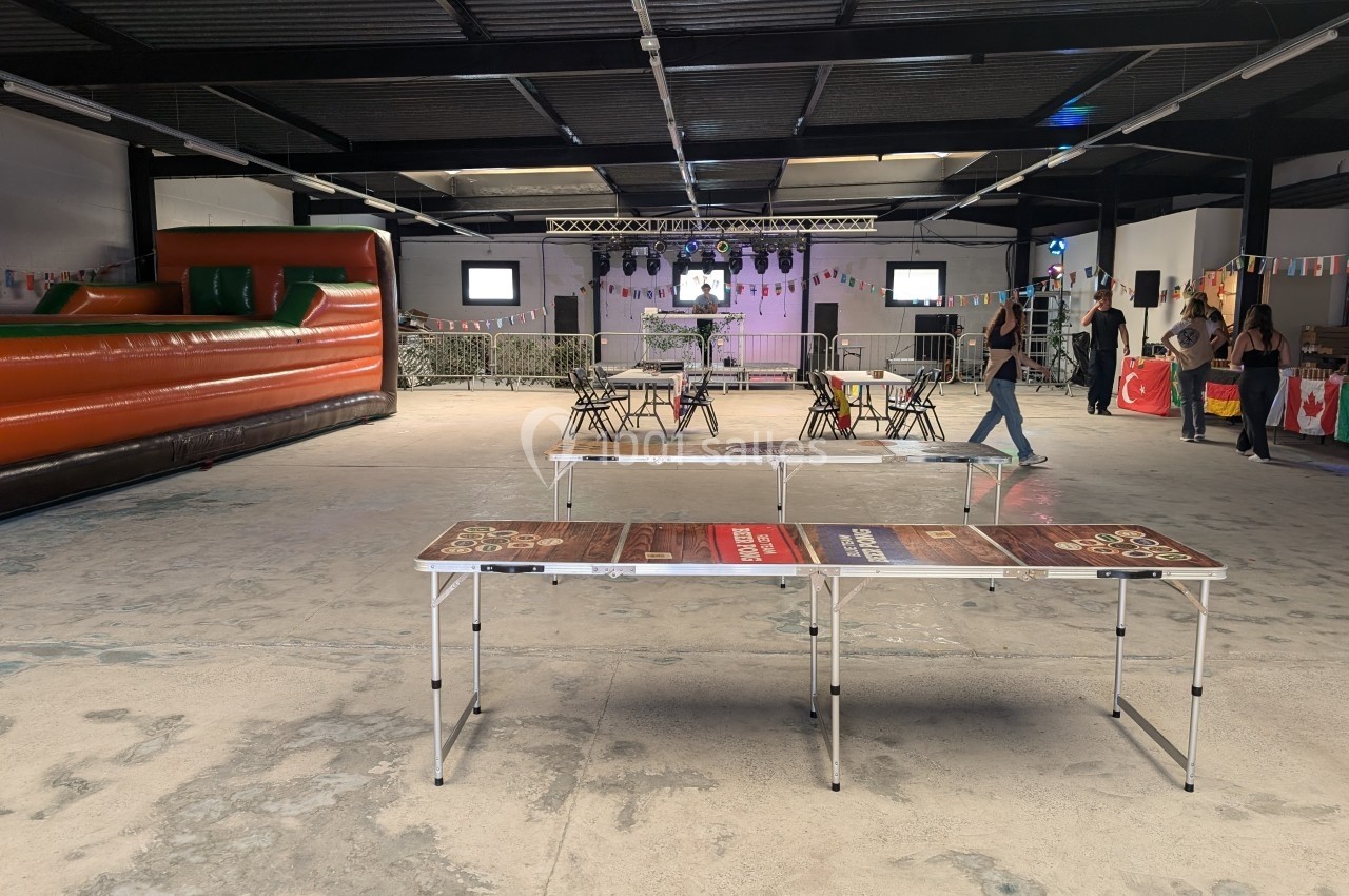 Salle événementielle avec tables pliantes, château gonflable, décorations et quelques personnes en arrière-plan.