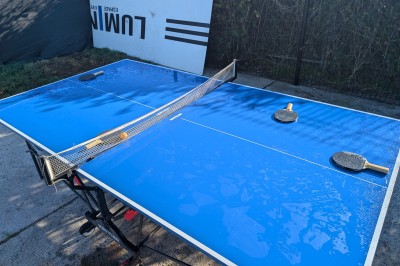 Des enfants colorient des dessins autour d'une table ronde, entourés d'adultes dans un espace intérieur animé.