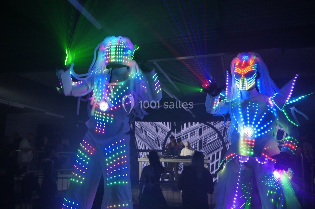 Deux personnes en costumes lumineux à LED colorés dans un environnement sombre, avec des faisceaux laser.