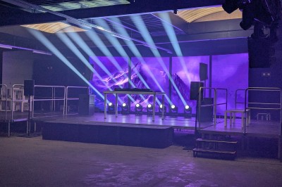 Des enfants colorient des dessins autour d'une table ronde, entourés d'adultes dans un espace intérieur animé.