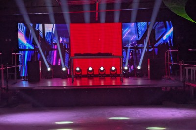 Des enfants colorient des dessins autour d'une table ronde, entourés d'adultes dans un espace intérieur animé.