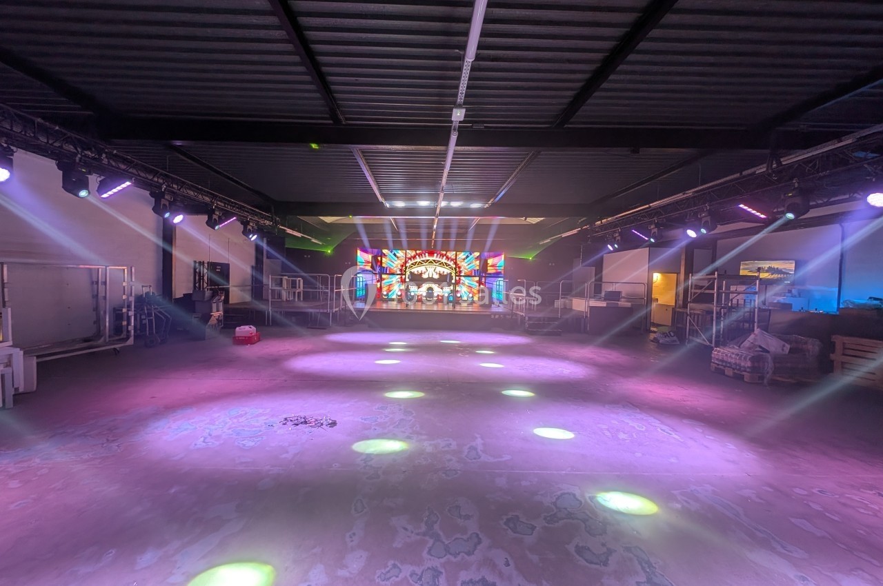 Salle industrielle avec éclairage coloré, projecteurs au sol et écran lumineux affichant un motif coloré en arrière-plan.