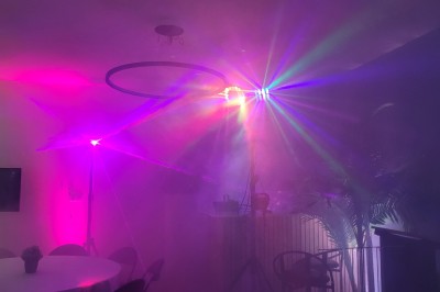 Des enfants colorient des dessins autour d'une table ronde, entourés d'adultes dans un espace intérieur animé.