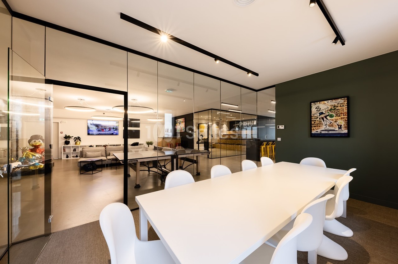 Salle de réunion moderne avec table blanche, chaises design et vue sur un espace ouvert avec murs en verre.