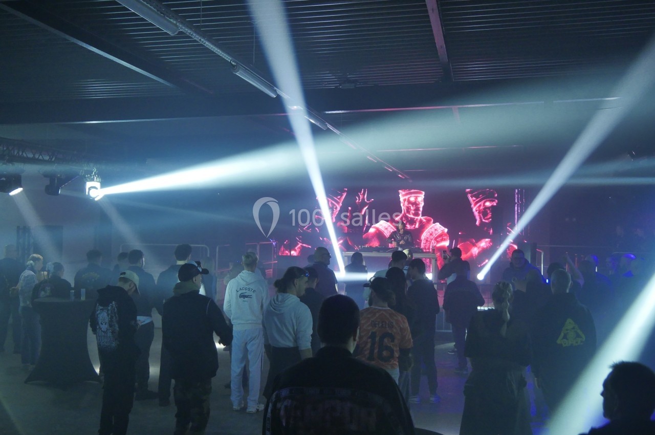 Groupe de personnes dans une salle sombre avec des jeux de lumière et un écran affichant des visuels rouges en arrière-plan.