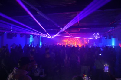 Des enfants colorient des dessins autour d'une table ronde, entourés d'adultes dans un espace intérieur animé.