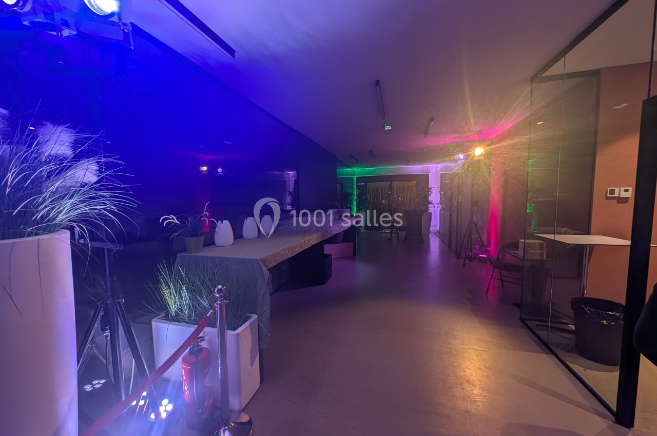 Salle moderne avec éclairage coloré, table longue décorée et plantes en pots, ambiance événementielle.