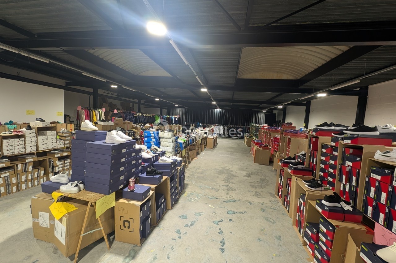 Entrepôt avec des étagères et des piles de boîtes de chaussures, entourées de vêtements et d'autres articles.