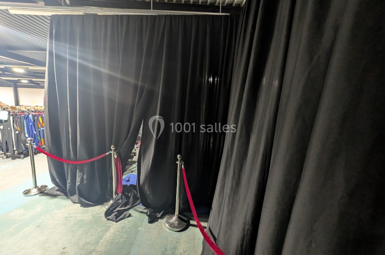 Rideaux noirs ouverts dans un espace industriel, délimitant une zone avec des cordons rouges et poteaux chromés.