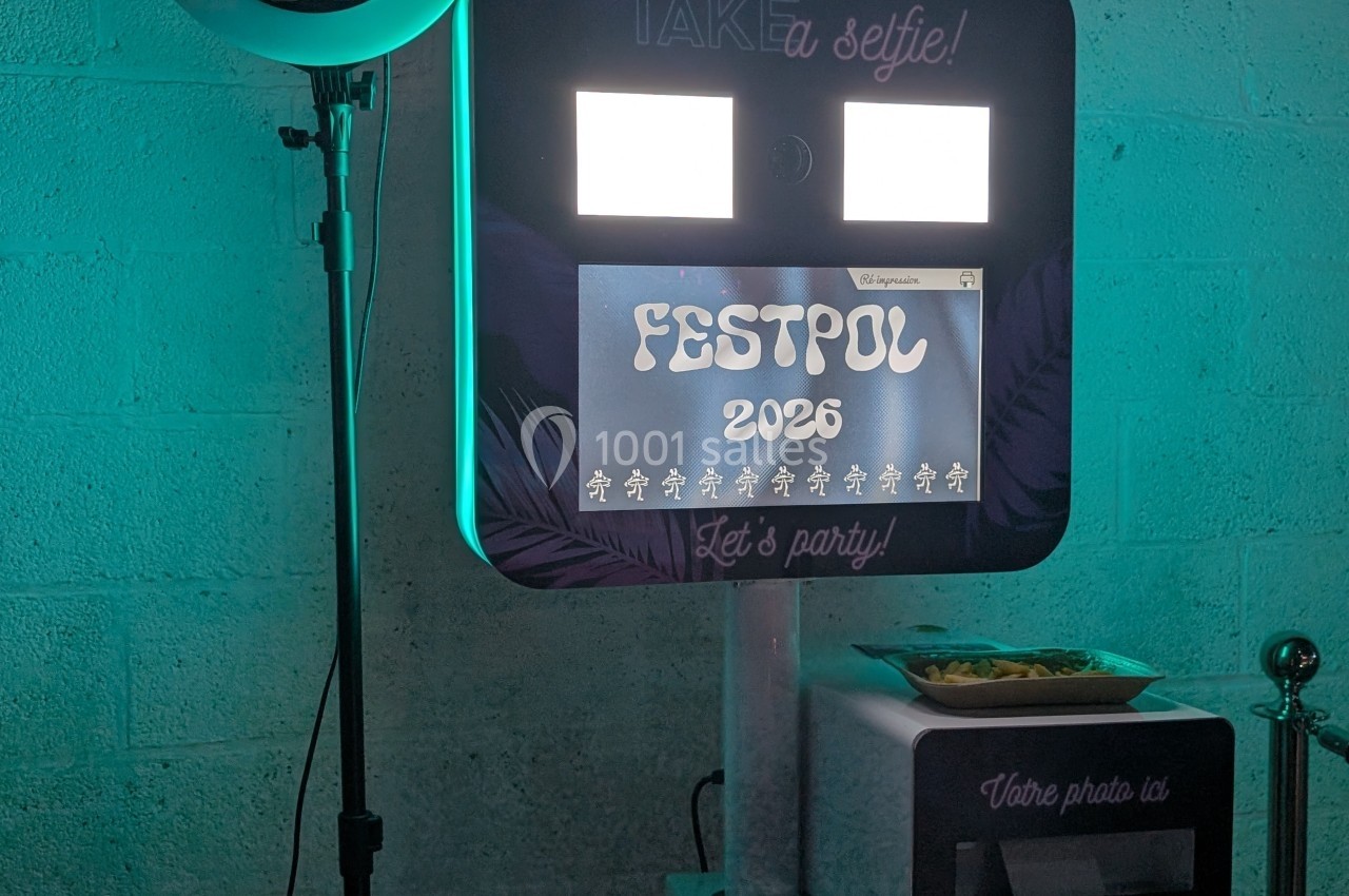 Borne photo rétroéclairée avec l'inscription ’Festpol 2026’, posée contre un mur en béton, entourée d'accessoires.