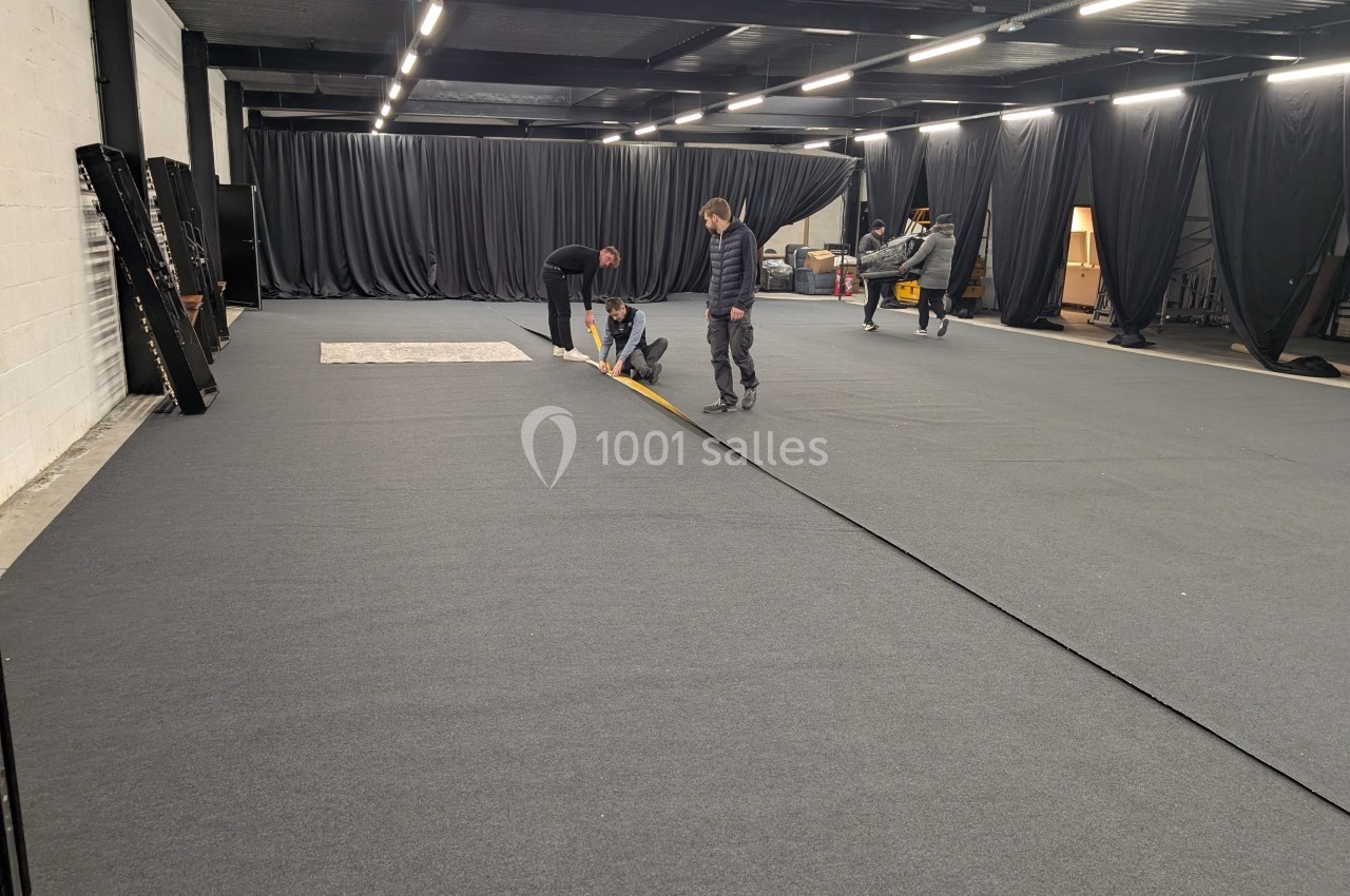 Des personnes installent un revêtement de sol gris dans un grand espace intérieur avec des rideaux noirs.