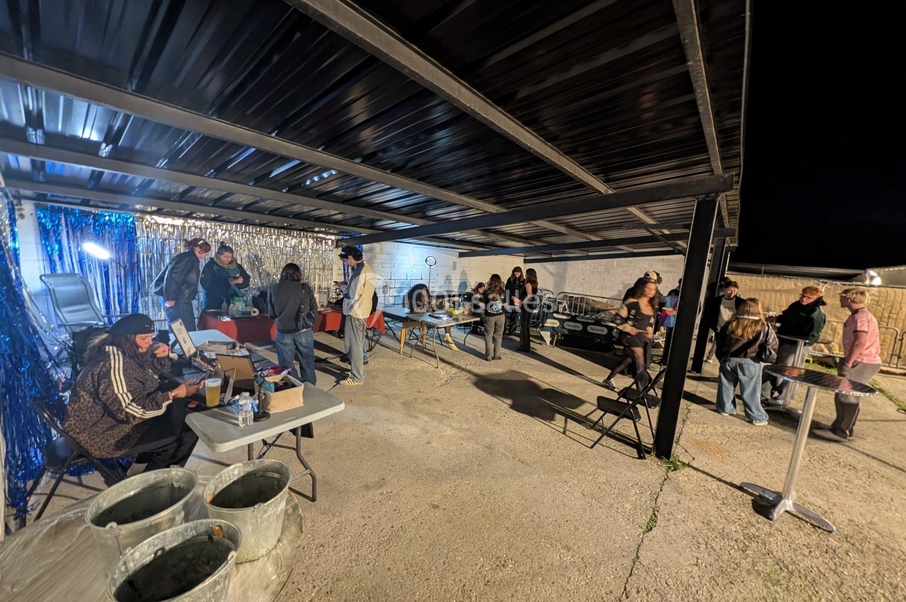 Des personnes rassemblées sous un abri en soirée, discutant et participant à des activités sur des tables installées.