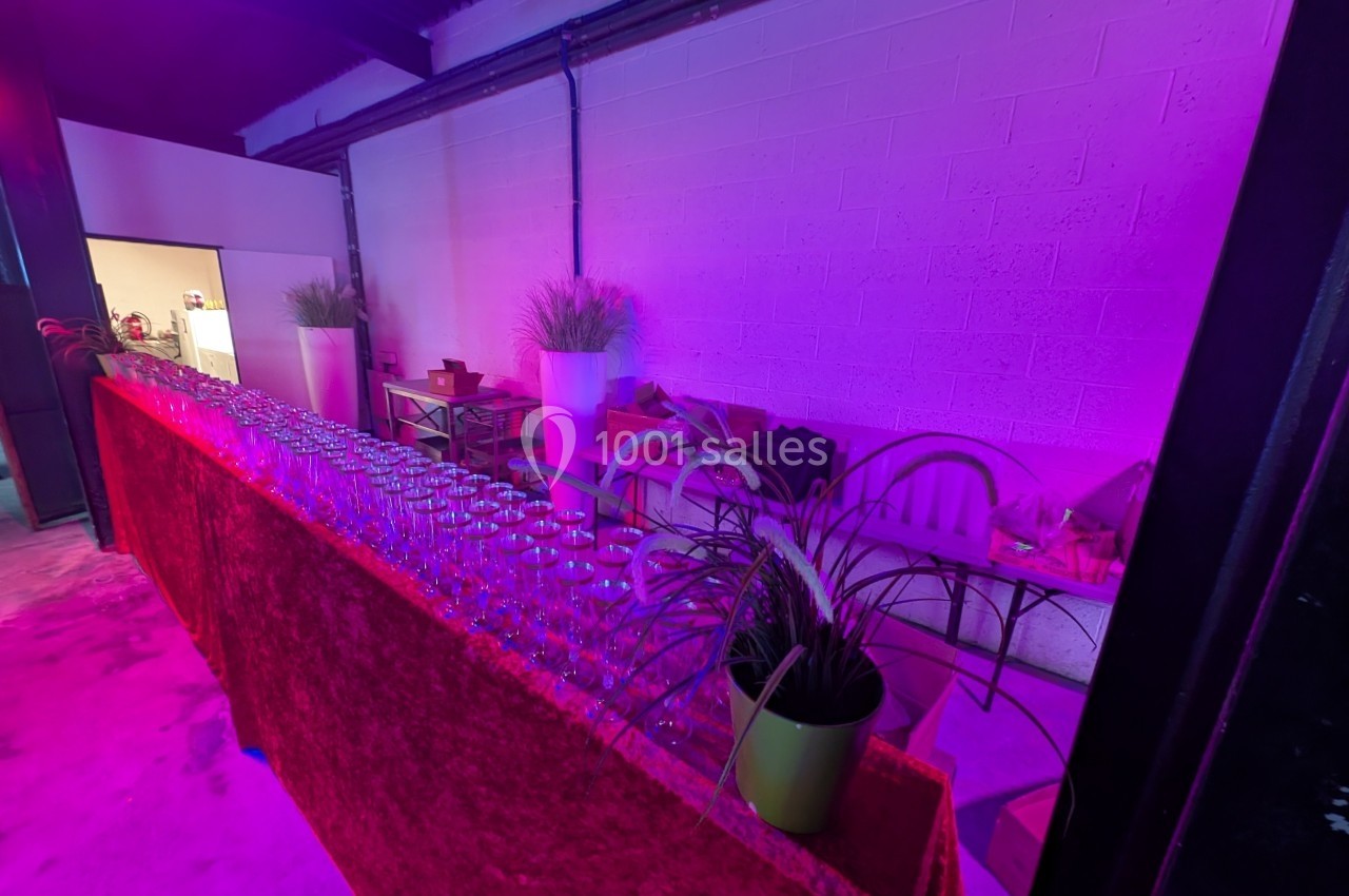 Table avec rangée de verres vides et décorations végétales dans une pièce éclairée par une lumière violette.