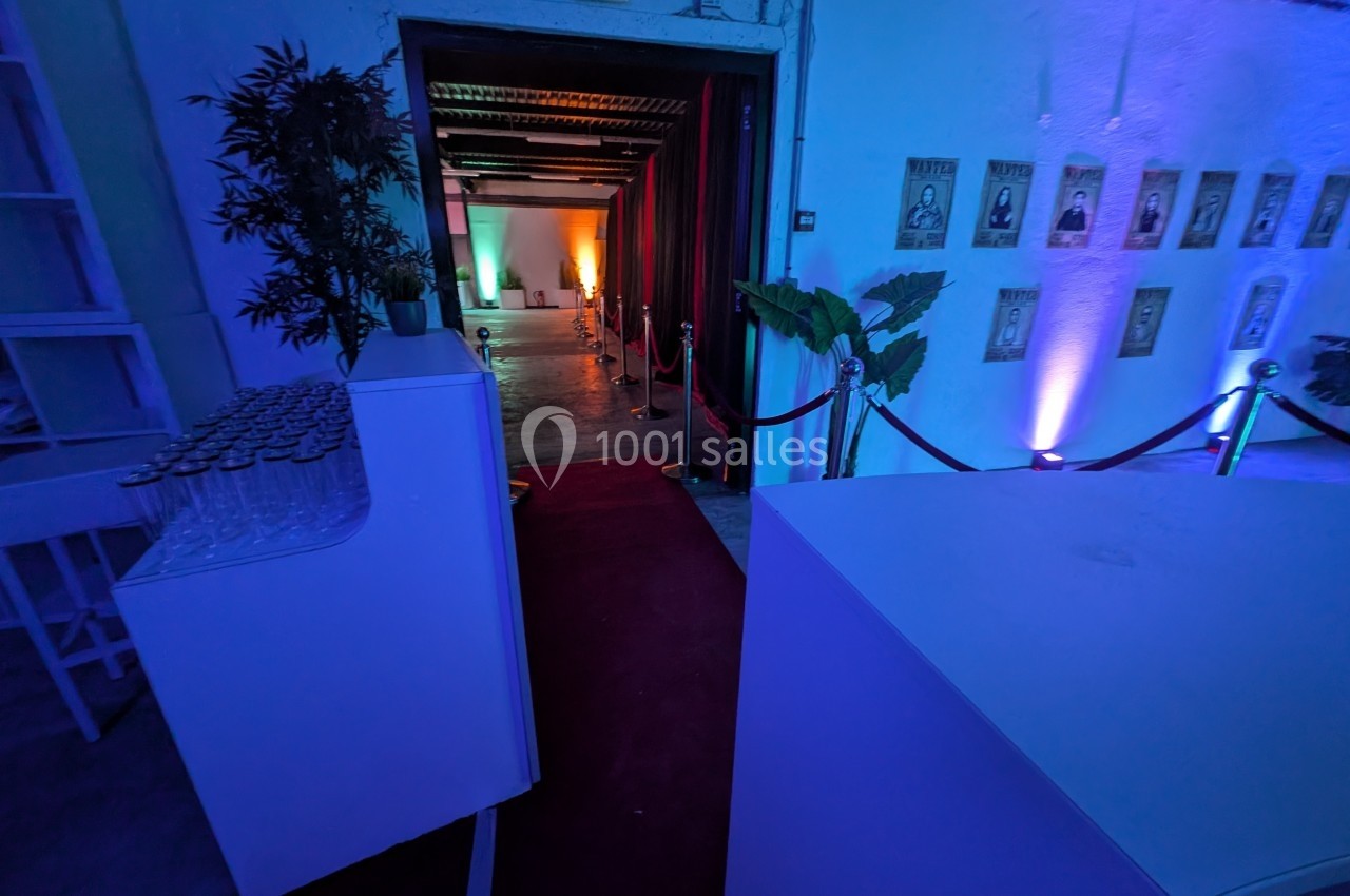 Entrée d'une salle éclairée par des lumières colorées, avec tapis rouge, cordons de sécurité et décorations murales.