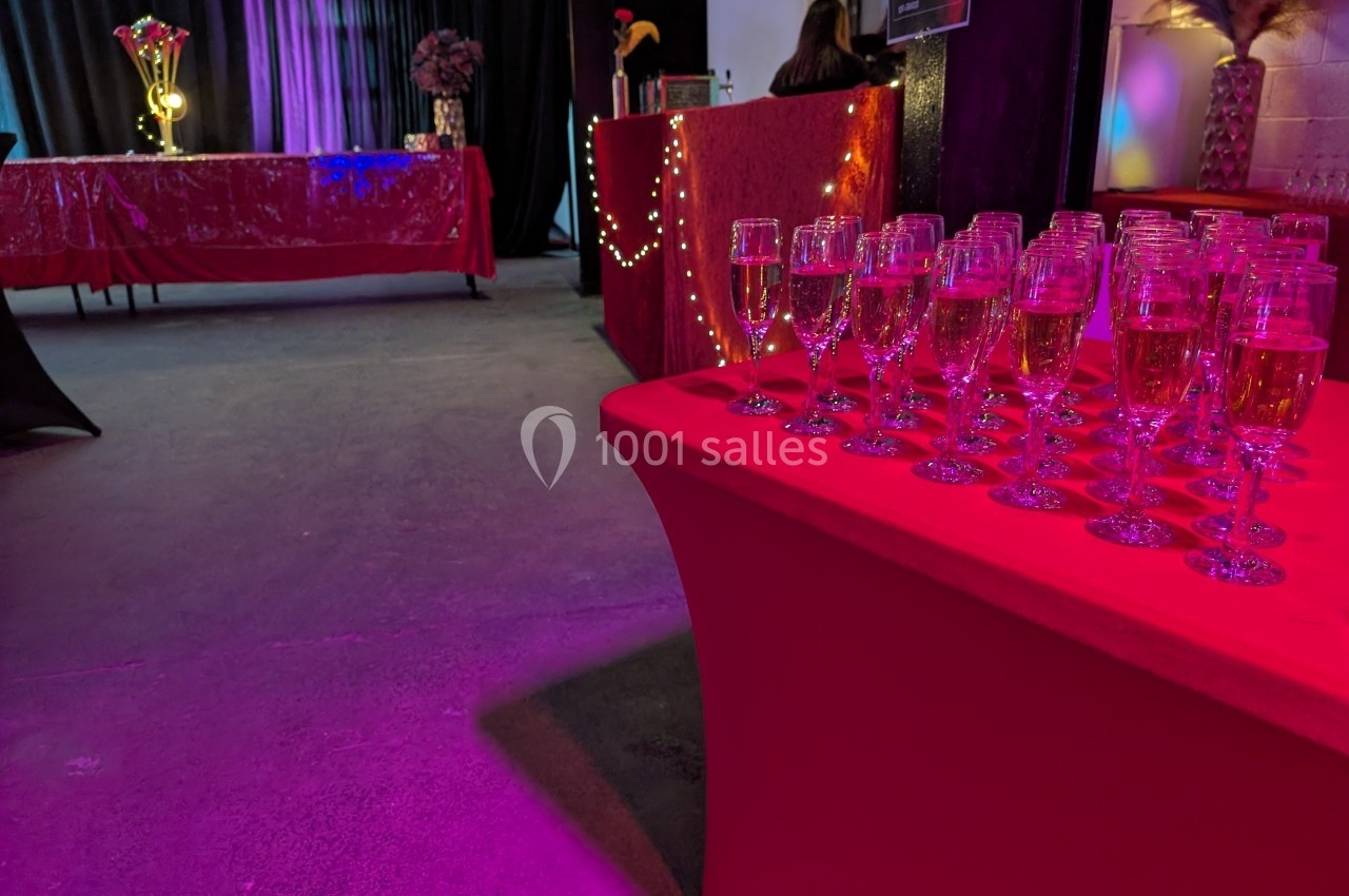 Verres de champagne alignés sur une table rouge dans une salle décorée avec des lumières et des nappes rouges.