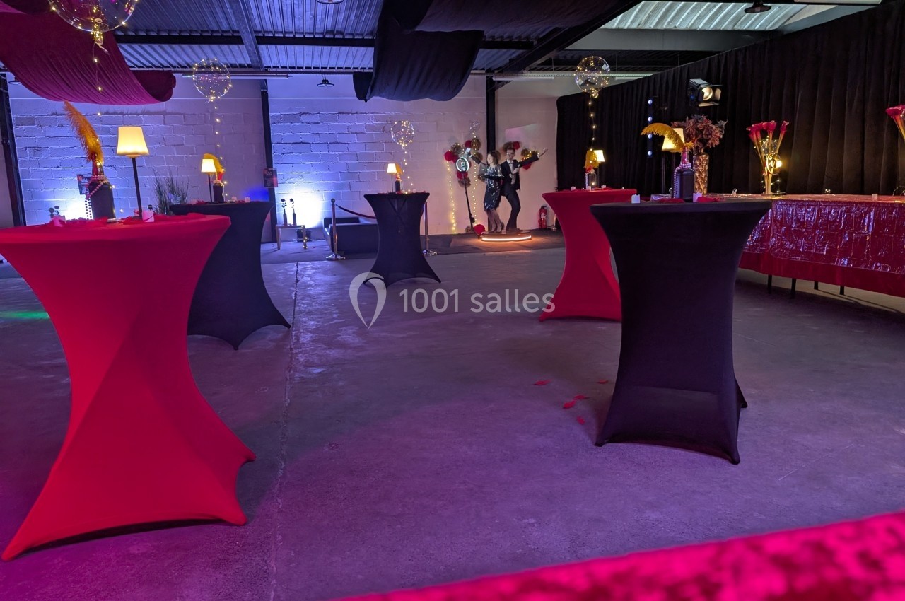 Salle décorée pour un événement avec des tables hautes recouvertes de nappes rouges et noires, éclairage tamisé.