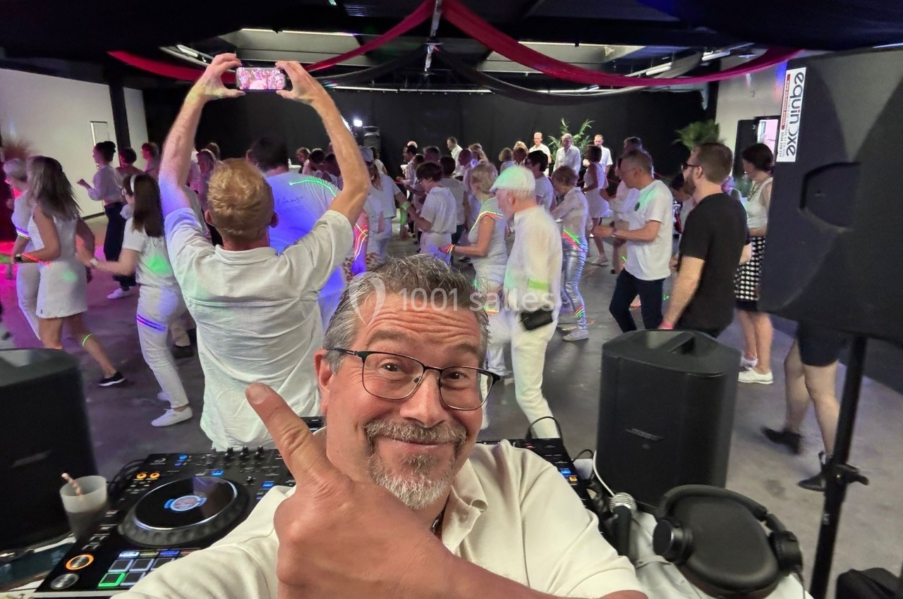 Un DJ souriant devant une piste de danse animée avec des participants vêtus de blanc.