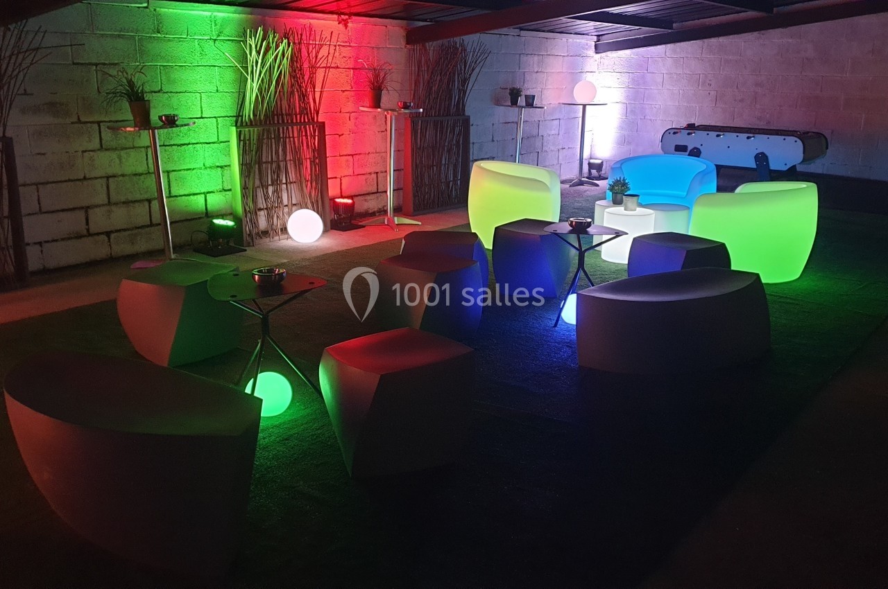 Espace intérieur avec mobilier lumineux coloré, tables basses et décoration moderne dans une ambiance tamisée.
