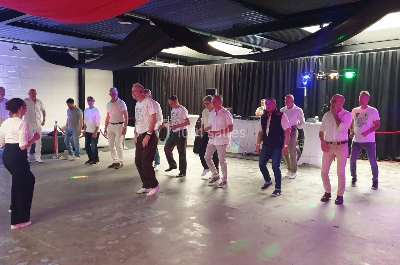 Groupe de personnes en tenue décontractée dans une salle, pratiquant une danse en ligne sous des éclairages colorés.