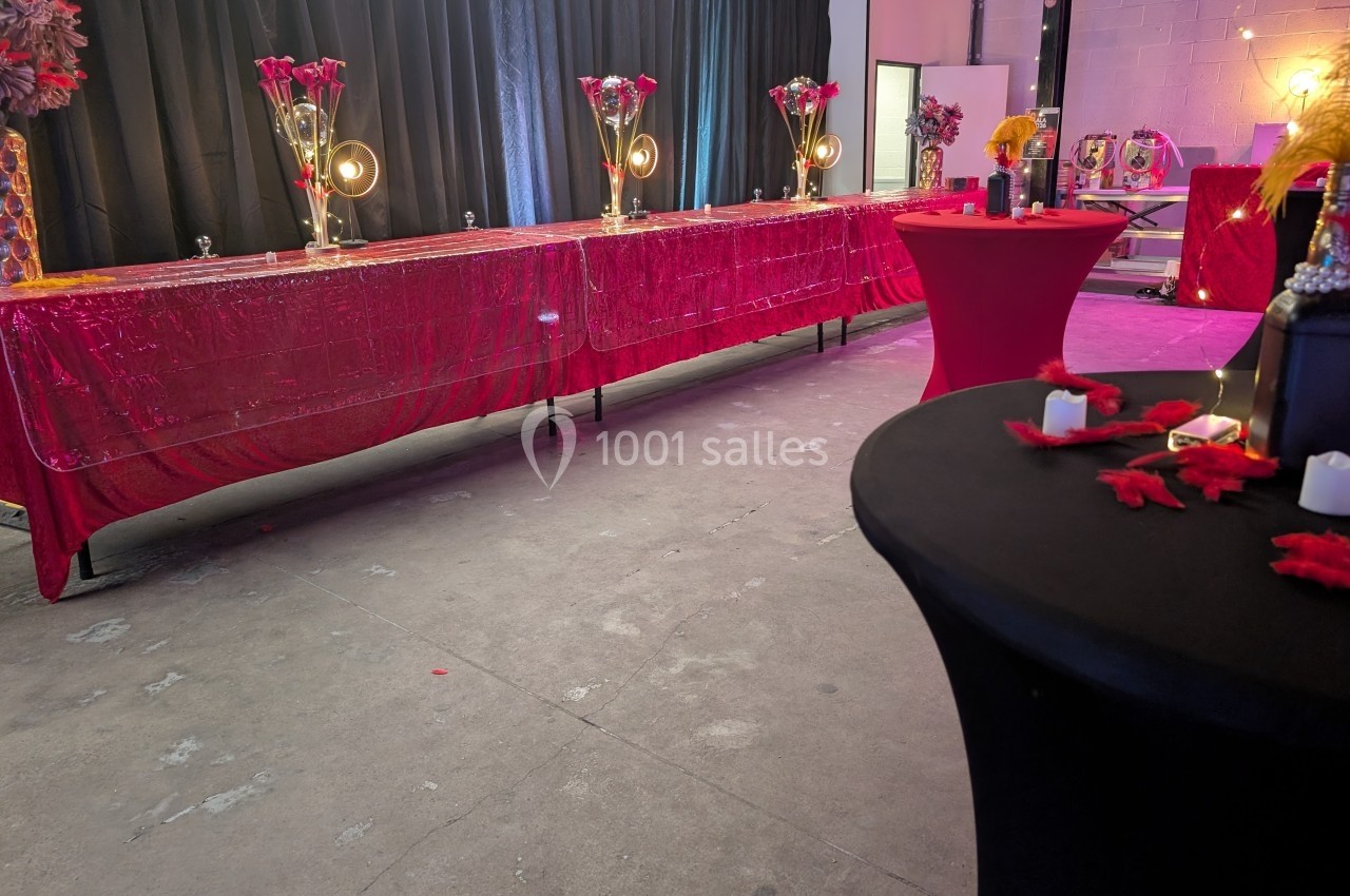 Salle décorée avec des nappes rouges, des vases fleuris, des bougies et des tables hautes pour un événement festif.